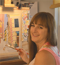 This is an image of Joanne Grant.  She is shown sitting in front of an easel painting an outdoor city scene.  She is shown from her shoulders upward.  She is smiling and has long brown hair and bangs.
