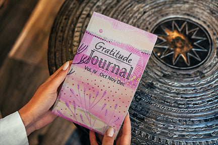 This image contains hands holding a gratitude journal by joanne grant art.  This gratitude journal is volume 4 and the cover image is a painting by joanne grant that is a pink and peach whimsical coral reef.